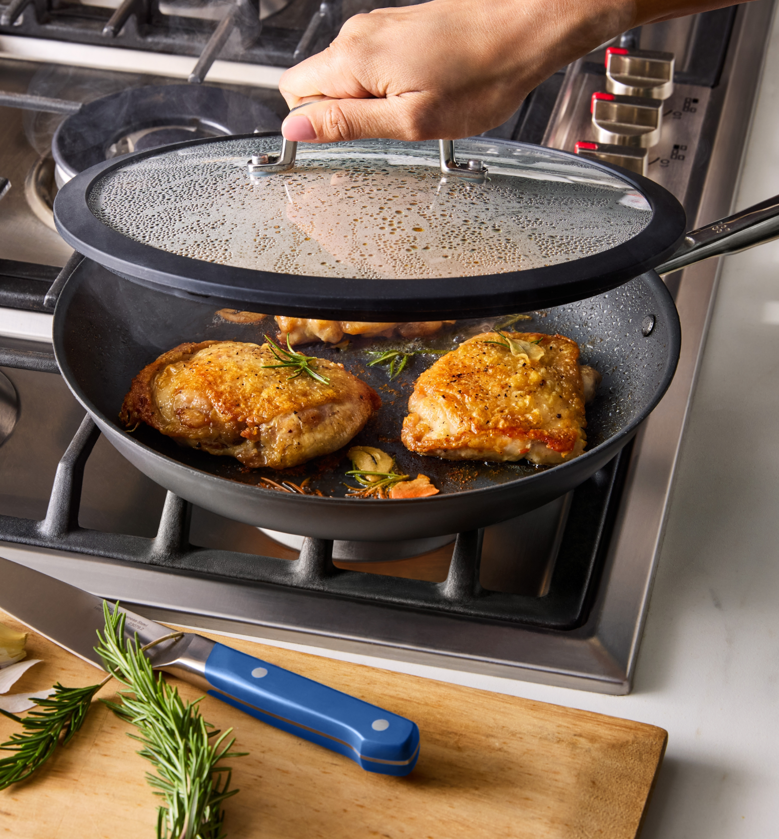 Golden brown pan-seared chicken thighs cooking in nonstick skillet with rosemary and garlic on gas stove