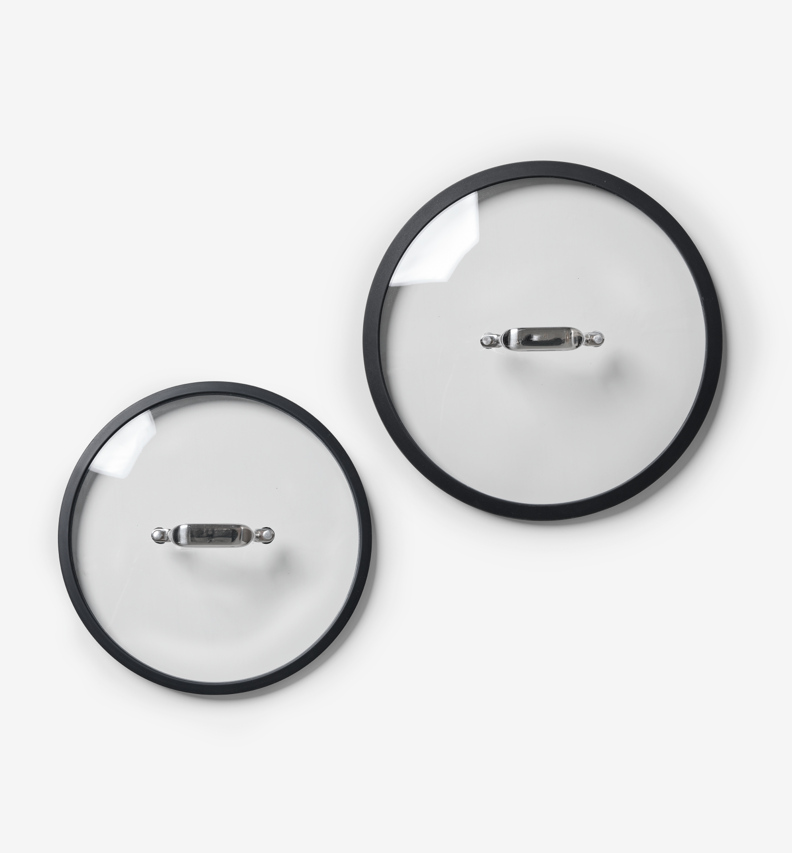 Two glass pot lids with black rim and stainless steel handles, top-down view